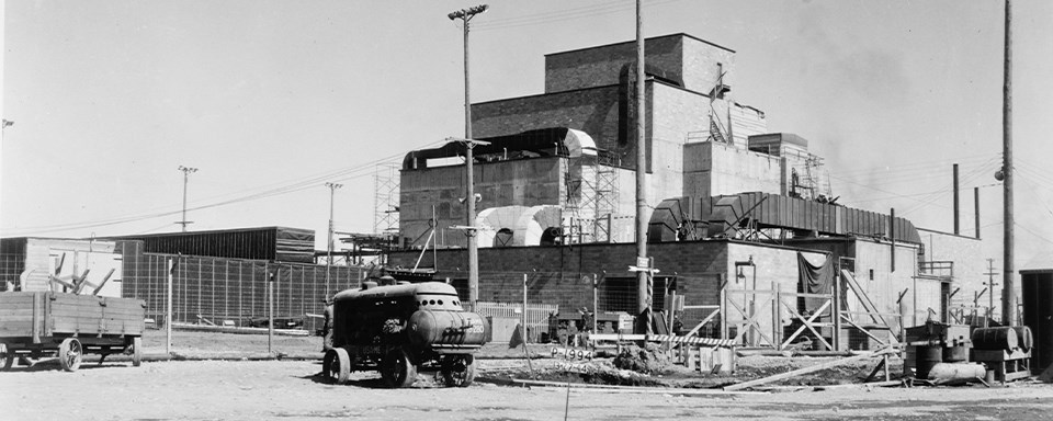 Black and white photo of a large, industrial building with a vehicle out front.