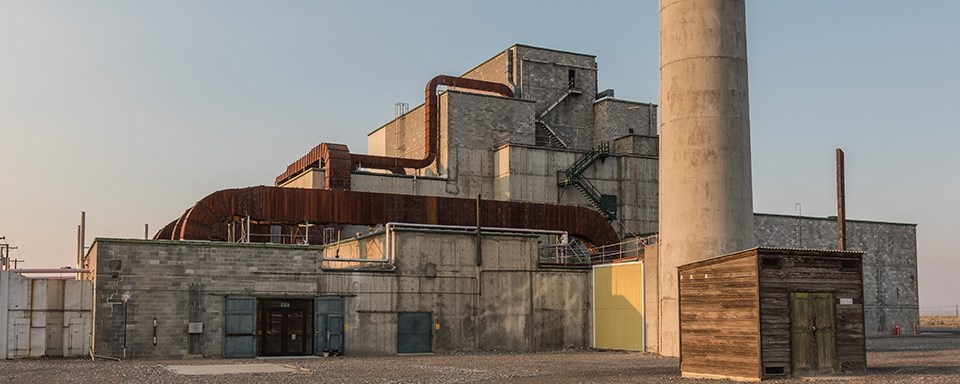Black and white photo of a large, industrial building with a vehicle out front.