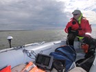 man in cold-weather gear standing in the back of a small boat loaded with scientific equipment