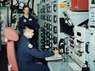 Uniformed Air Force Officers stand and sit in a room of electronic consoles