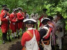 Soldiers in Red Coat and tricorn hats with heads bowed around a grave