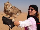 woman wearing black headscarf holding an owl on her outstretched gloved arm.