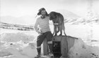 a man and sled dog sitting on a dog house, in a snowy landscape