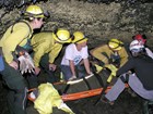 cave rescue crew in safety gear prepares to lift a person on a backboard litter