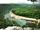Overlooking a bend in a river from the top of a stone cliff. Both banks are densely forested.
