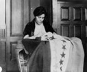 Woman sitting sewing flag with stars on it. 