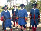 Three African American soldiers in blue uniforms and black tricorn hats smile at camera