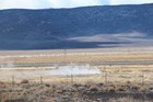 Steam rises from a small pond that sits in a desert setting void of much vegetation