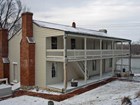 Two story building with a porch on the first and second floors; two red brick chimneys on the side.