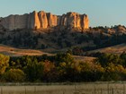 Buttes bathed in golden light of sunset, grassy field in foreground