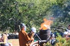 Flames emerging from metal barrel with several people standing around it with helmets.