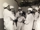 Woman in white lab coat and cap stands in the middle of five journalists inside the PUREX Plant.