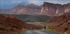 A landscape scene with a woman running down a deserted road with sandstone cliffs in the background.