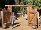 a woman stands in front of a tall wooden gate