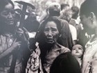 Black and white photo of two women holding religious items flanking distressed older woman in crowd