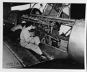 Black and white photo of a woman in coveralls working on an open plane
