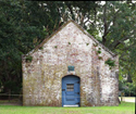 A white washed building of brick with a pitched roof and a blue arched door. 