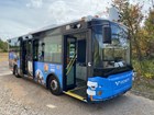 Blue and black electric vehicle sits parked in a gravel parking lot with trees in background