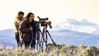 a group of people look through spotting scopes with a mountain in the background