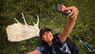 a person takes a selfie with a shed moose antler on the ground