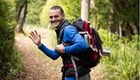 a man with backpack smiles and waves on a trail
