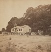 A schoolhouse surrounded by trees with a group of students standing in front.
