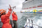 Two rangers in bright orange float coats wave to passengers on a nearby cruise ship.