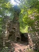 The ruins of a two-story stone house with a red brick chimney. Surrounded by green foliage.