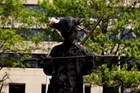 Dark bronze statue of a figure in a tri-corner hat looking down at a saber