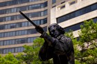 Dark bronze statue of a man sighting down the barrel of a rifle
