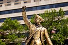 Gold toned statue of a man in a tri-corner hat raising a fist