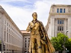 Gold toned statue of a man in a long cloak holding a tri-corner hat and an envelope