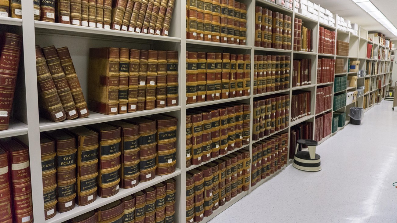 Tall bookcases line the length of the image, with white floors and flourescent lights