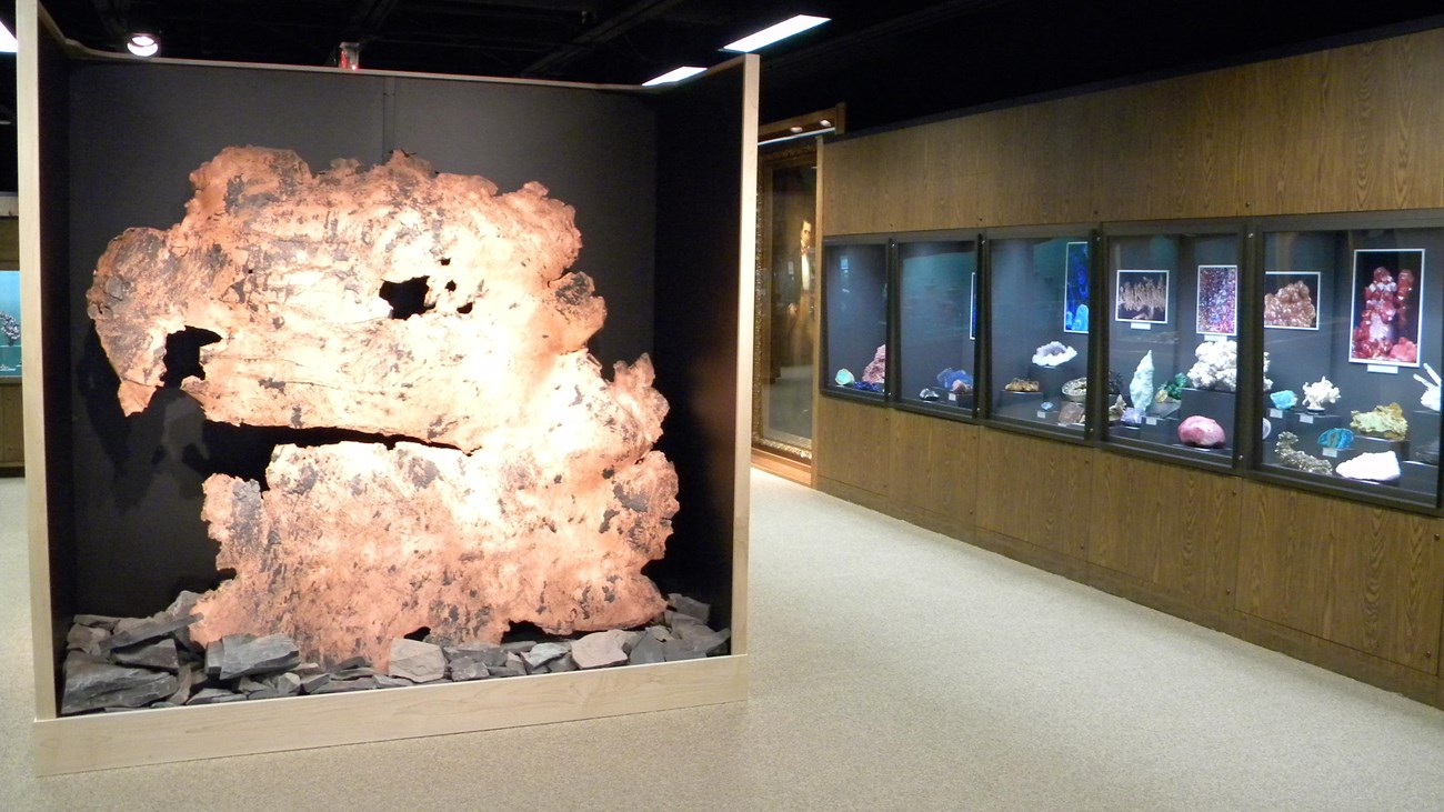 A Large piece of illuminated copper on the left as mineral displays in cabinets line the right.