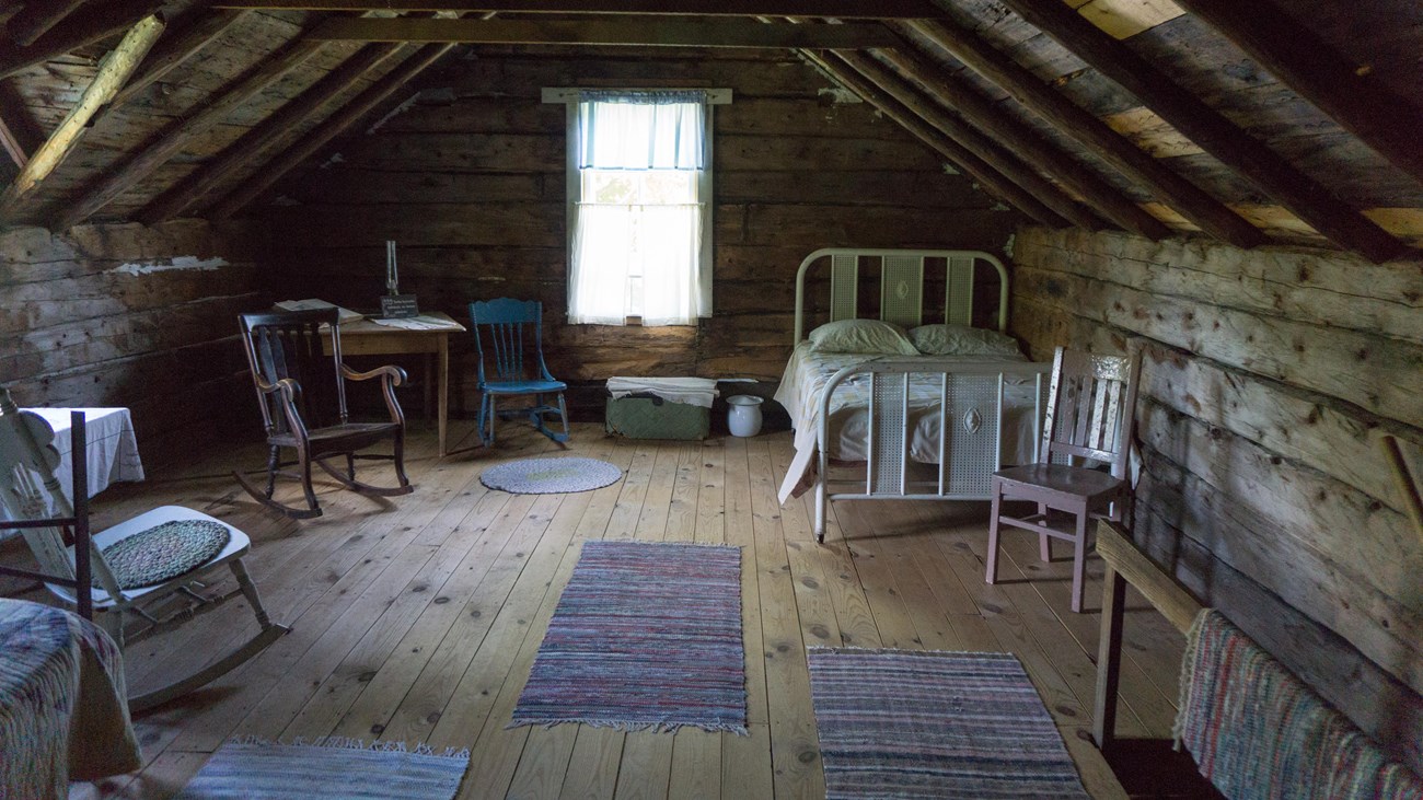 Antique chairs and beds in an attic with a single window and exposed rafters
