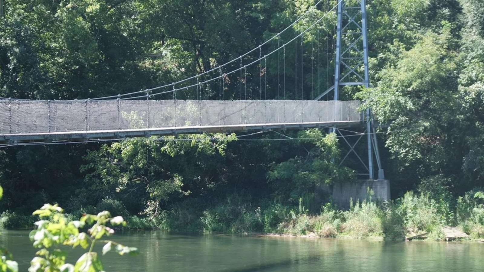 A suspension bridge over a river with trees on both sides.