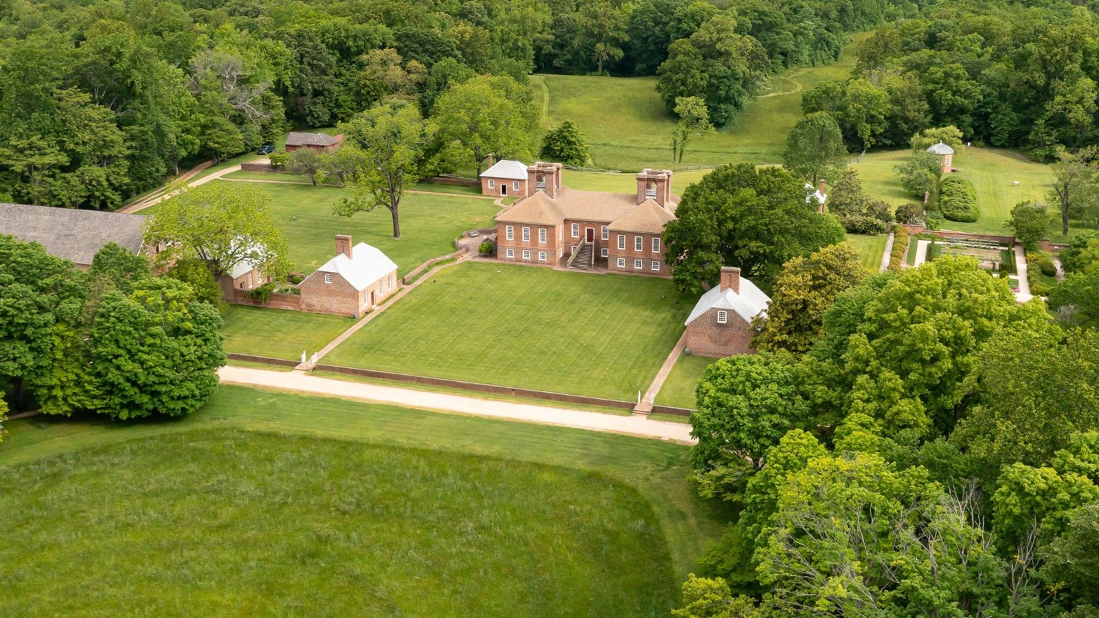 Aerial view of a brick mansion with surrounding lush greenery and distant water.
