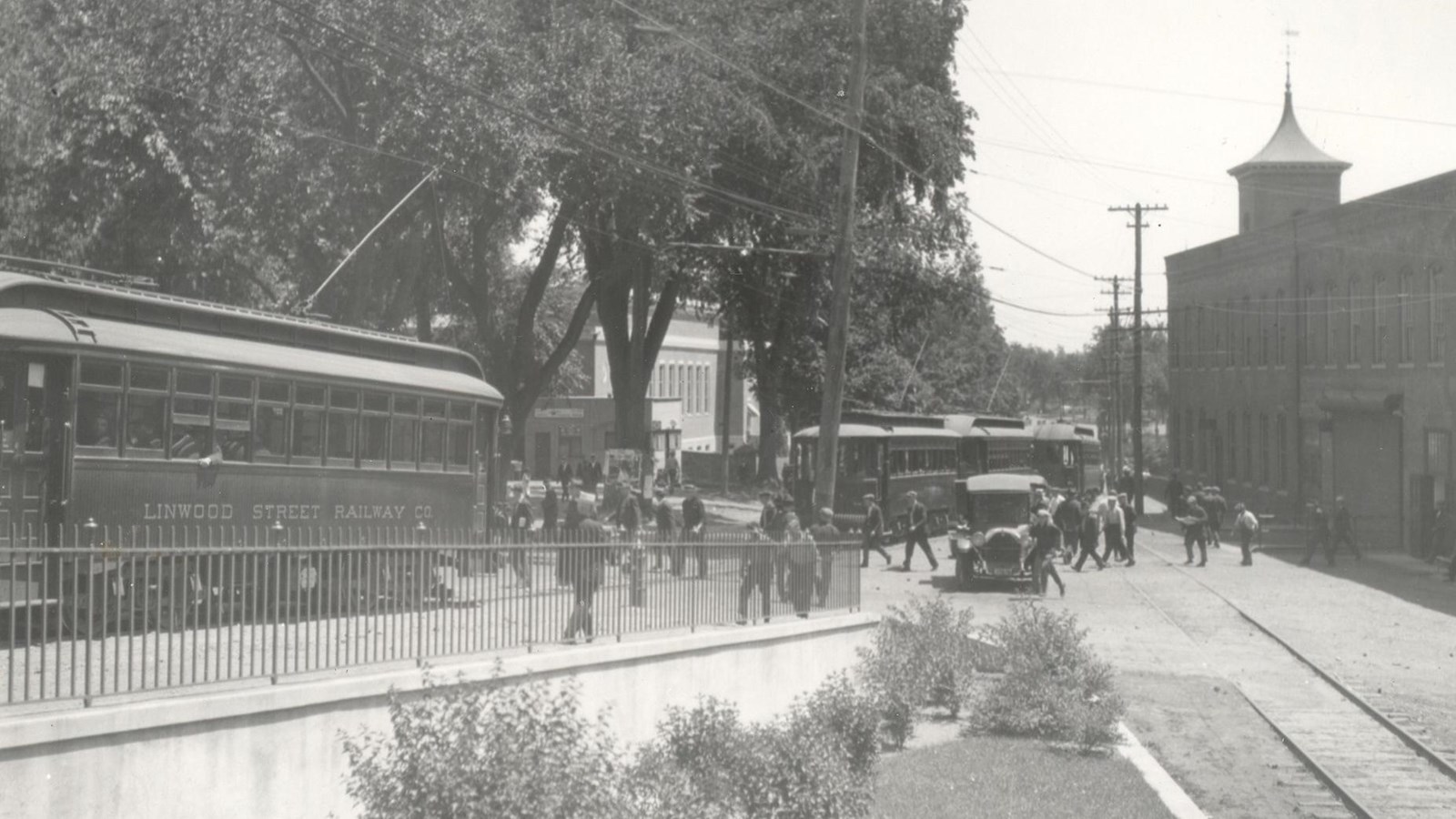 Historic photo showing mill on the right with trolley and people walking on the road. 