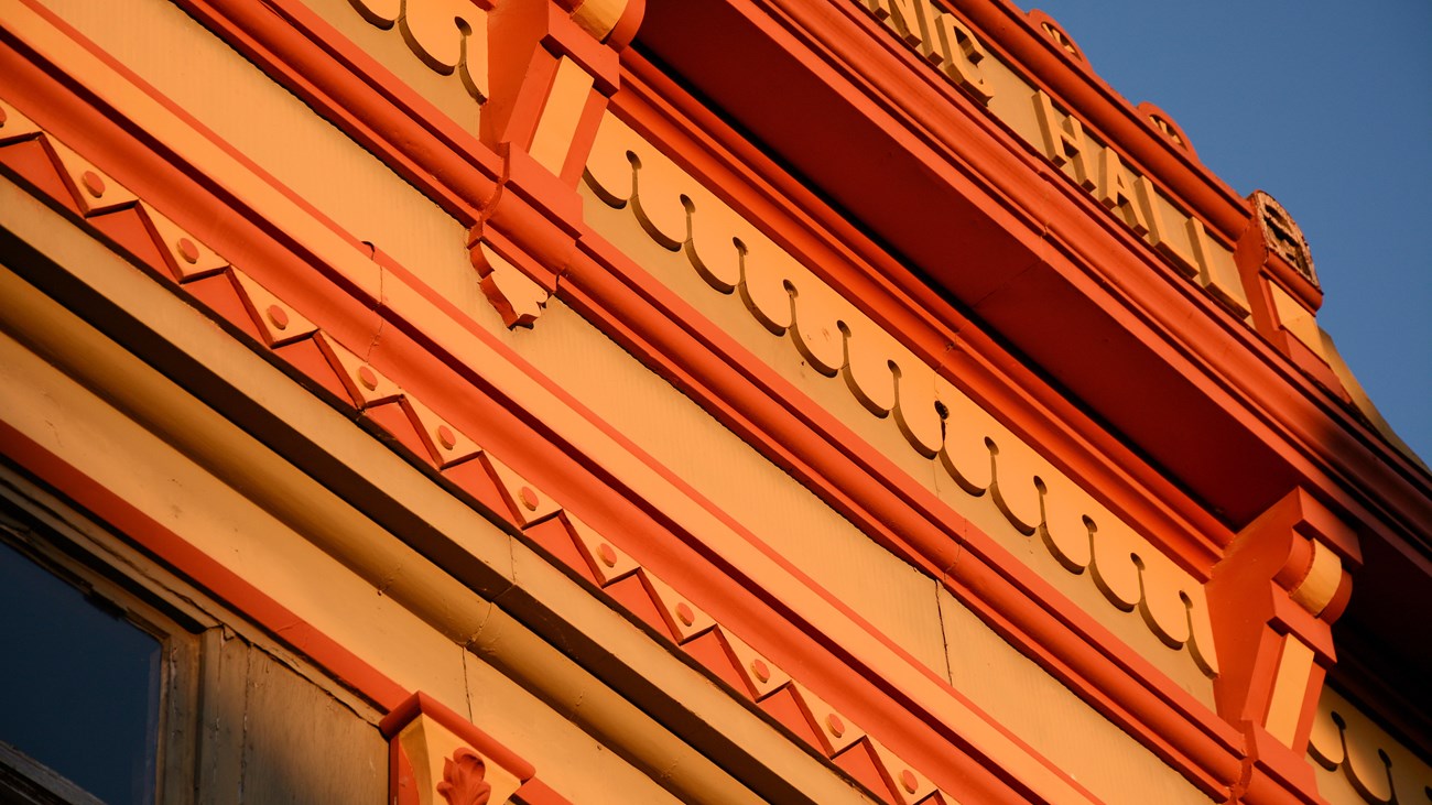 A detail photo of a building cornice shows courses of red and orange decorations.