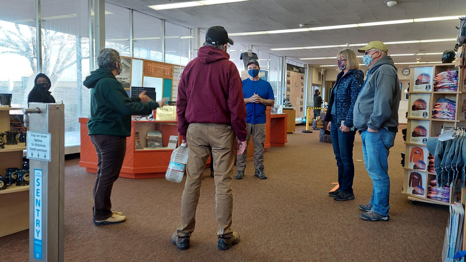 People gathered among displays of books and other items, large windows all around.