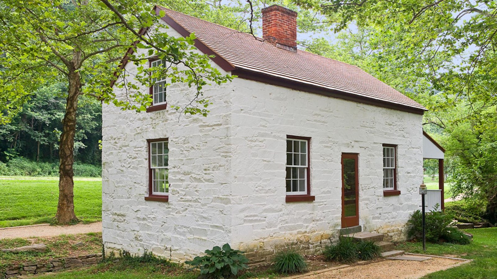 A white lockhouse with a rectangular base and A line roof sits on grass.