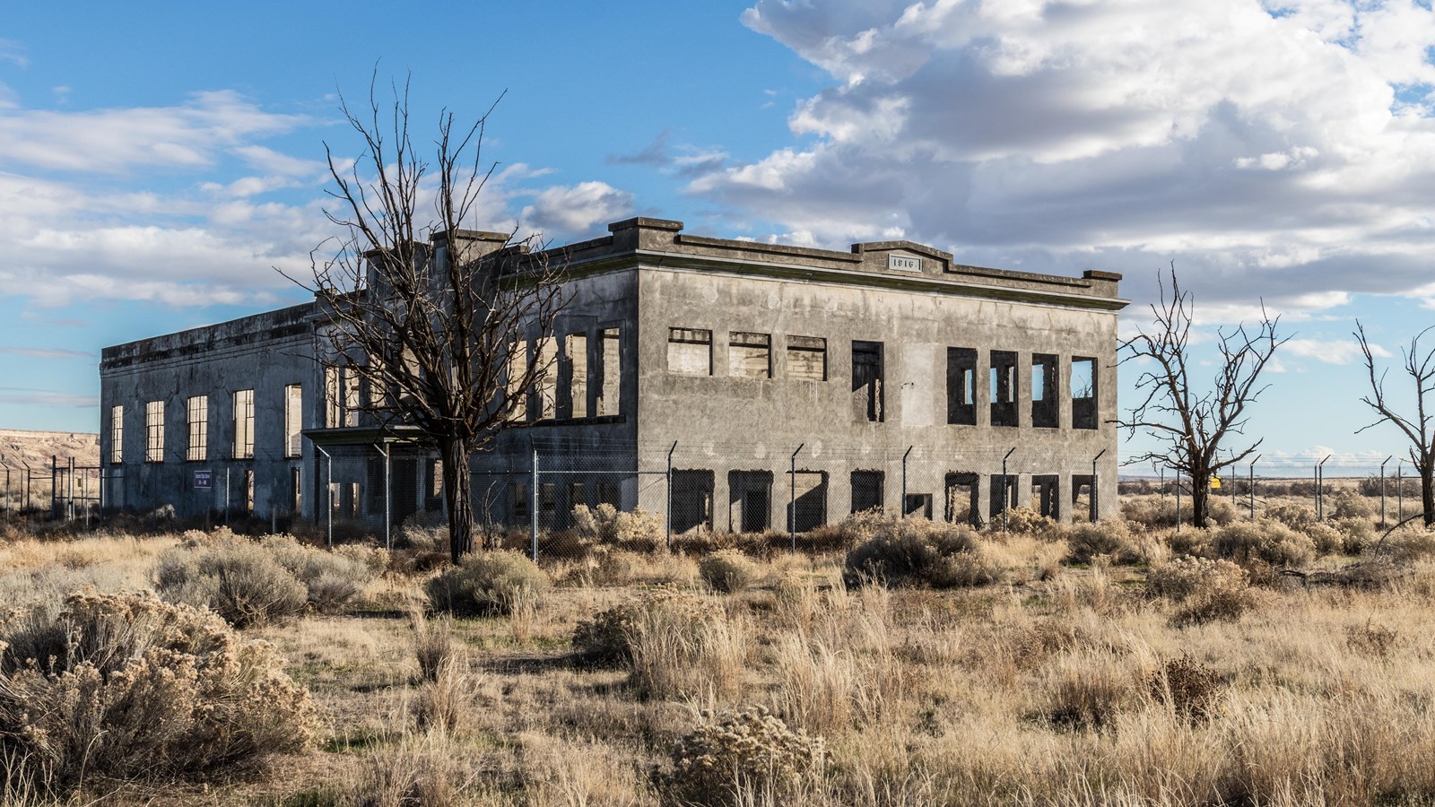 Color photograph of a large block neoclassical building in ruins surrounded by a fence