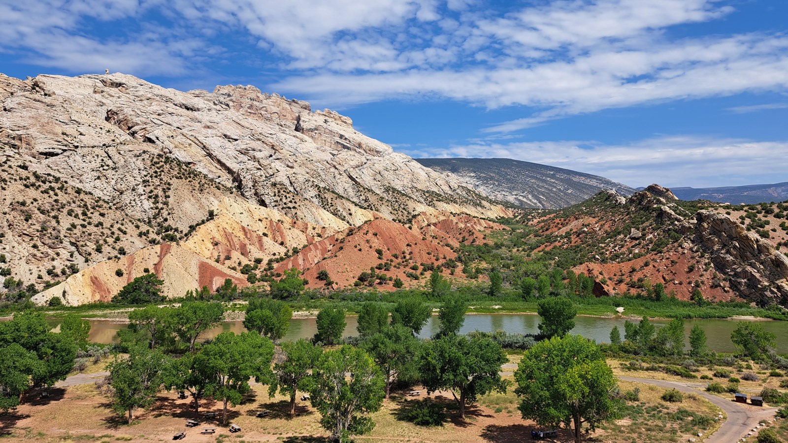 A panoramic view from a roadside pullout of a river flowing at the base of a desert mountain.