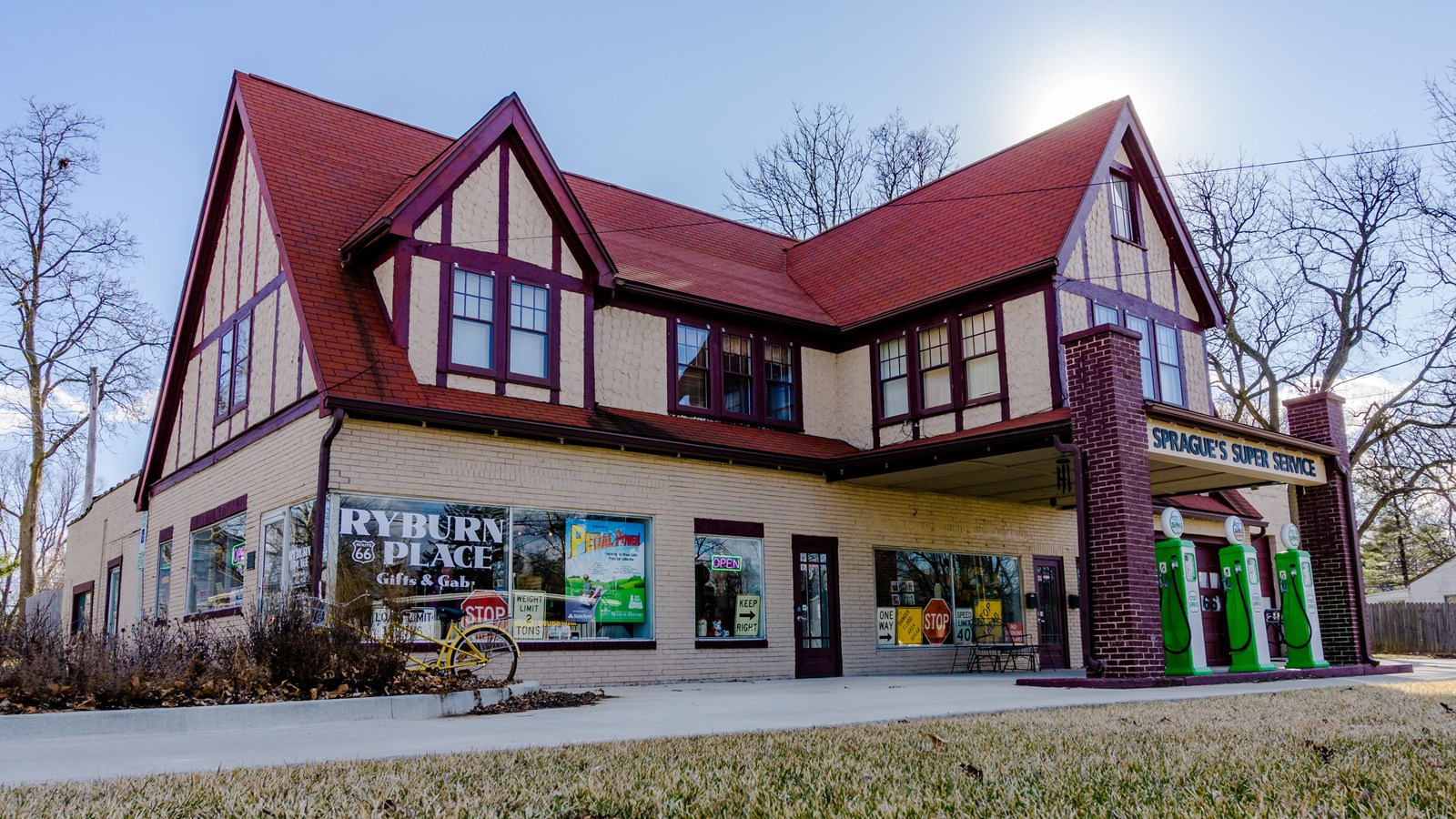 A large tan building with a steep, gabled red roof with three green old-fashioned gas pumps in front