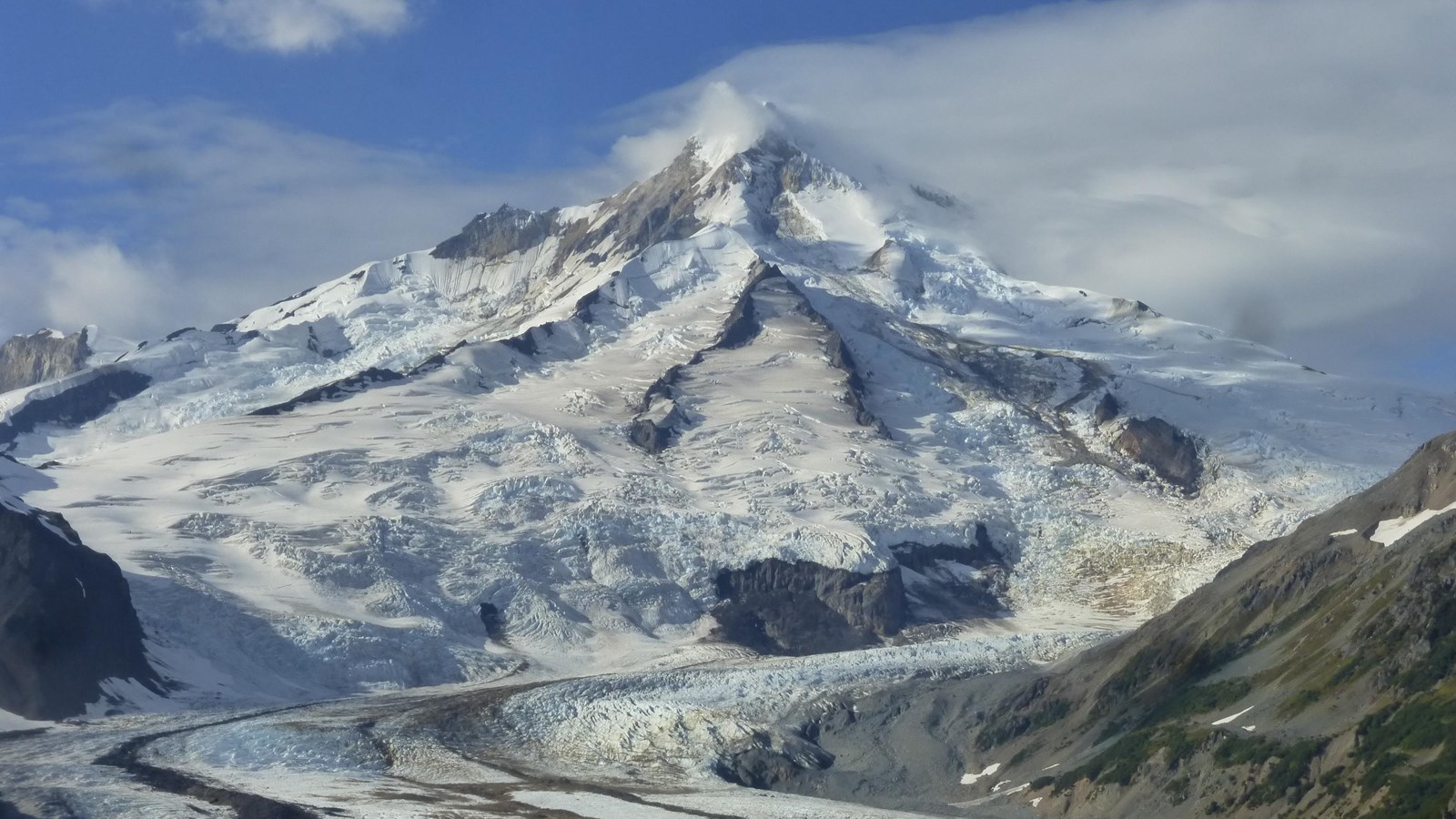 a cone-shaped volcano covered in snow and glaciers surrounded by tundra