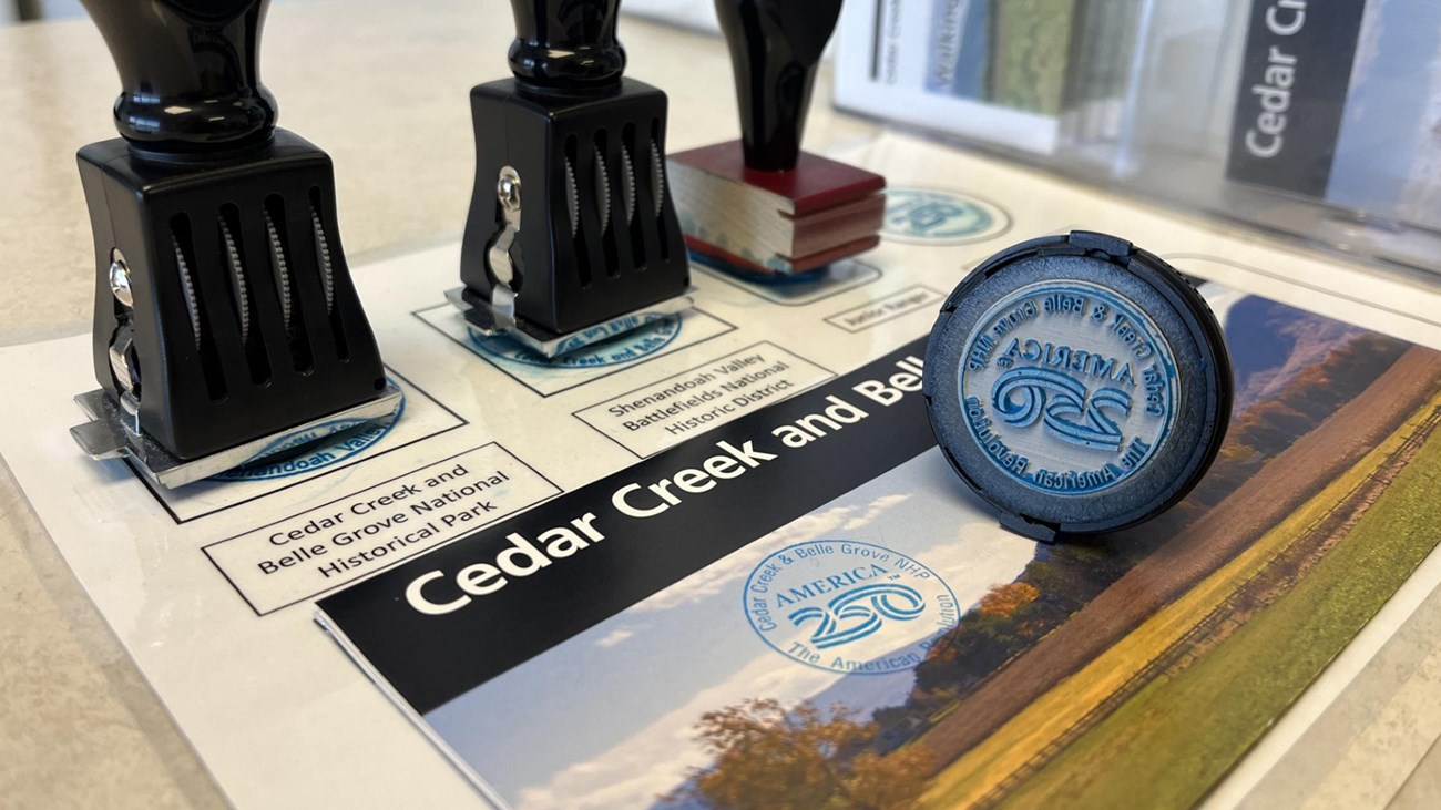 Three rubber stamps and a blue stamp pad on a brochure for Cedar Creek and Belle Grove National Hist
