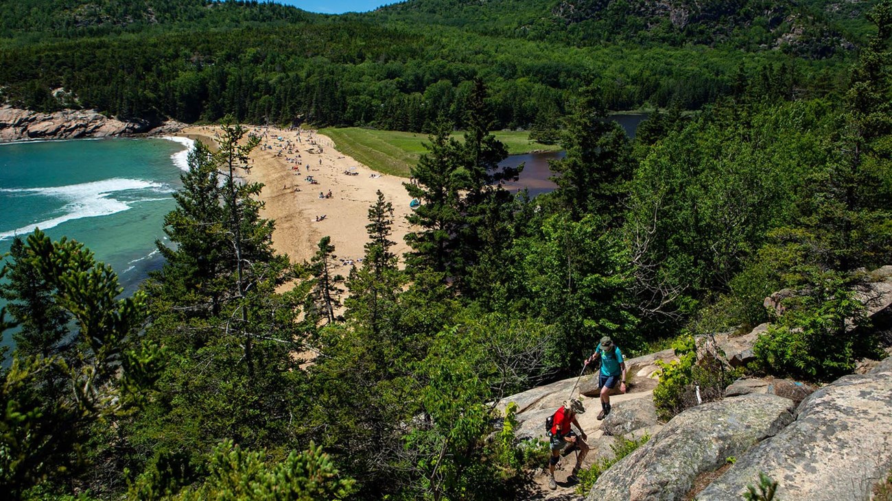 Two hikers walk along Great Head Trail overlooking Sand Beach.