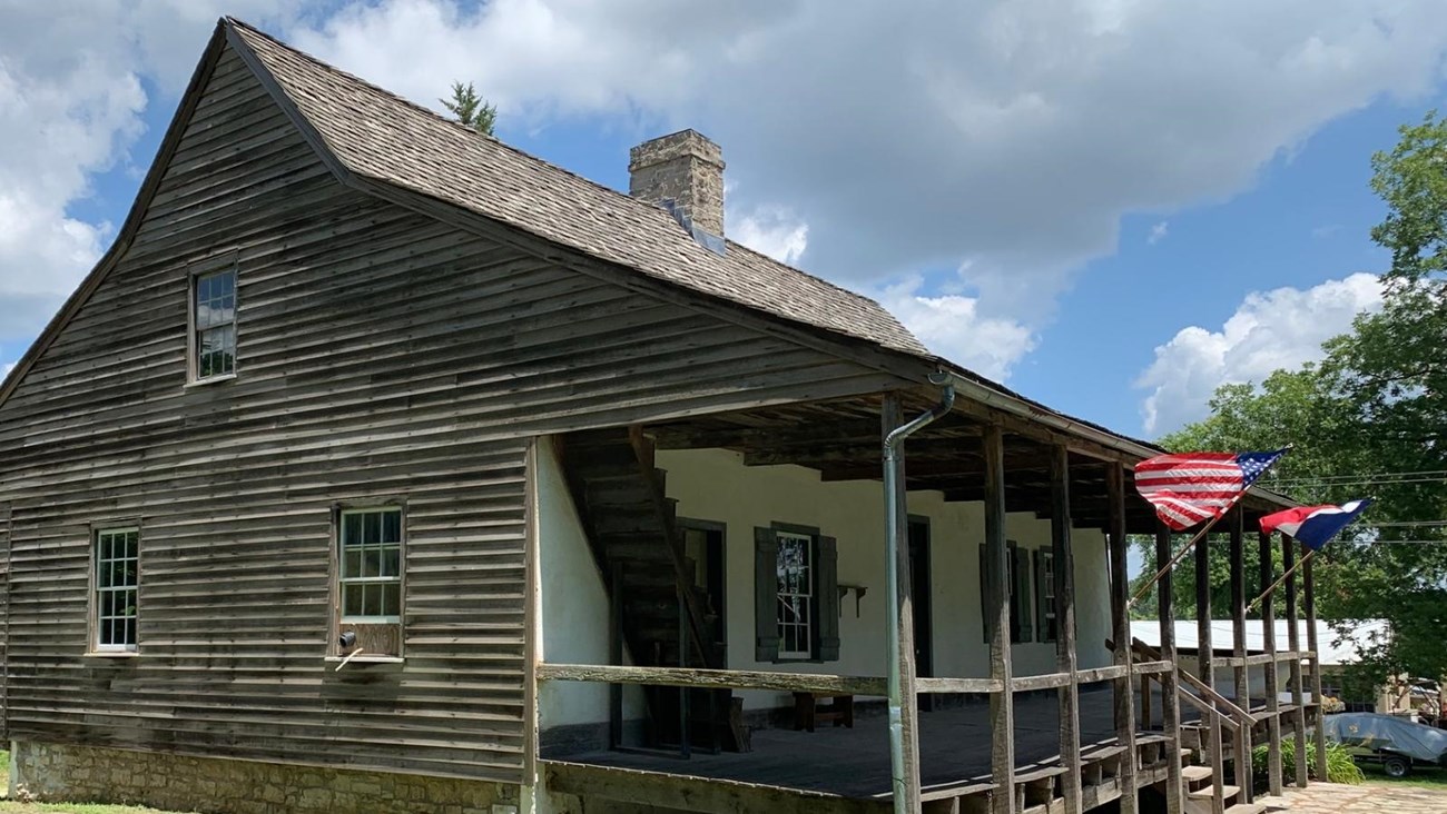 A historic home with a large front porch on which the American and French flags are flying