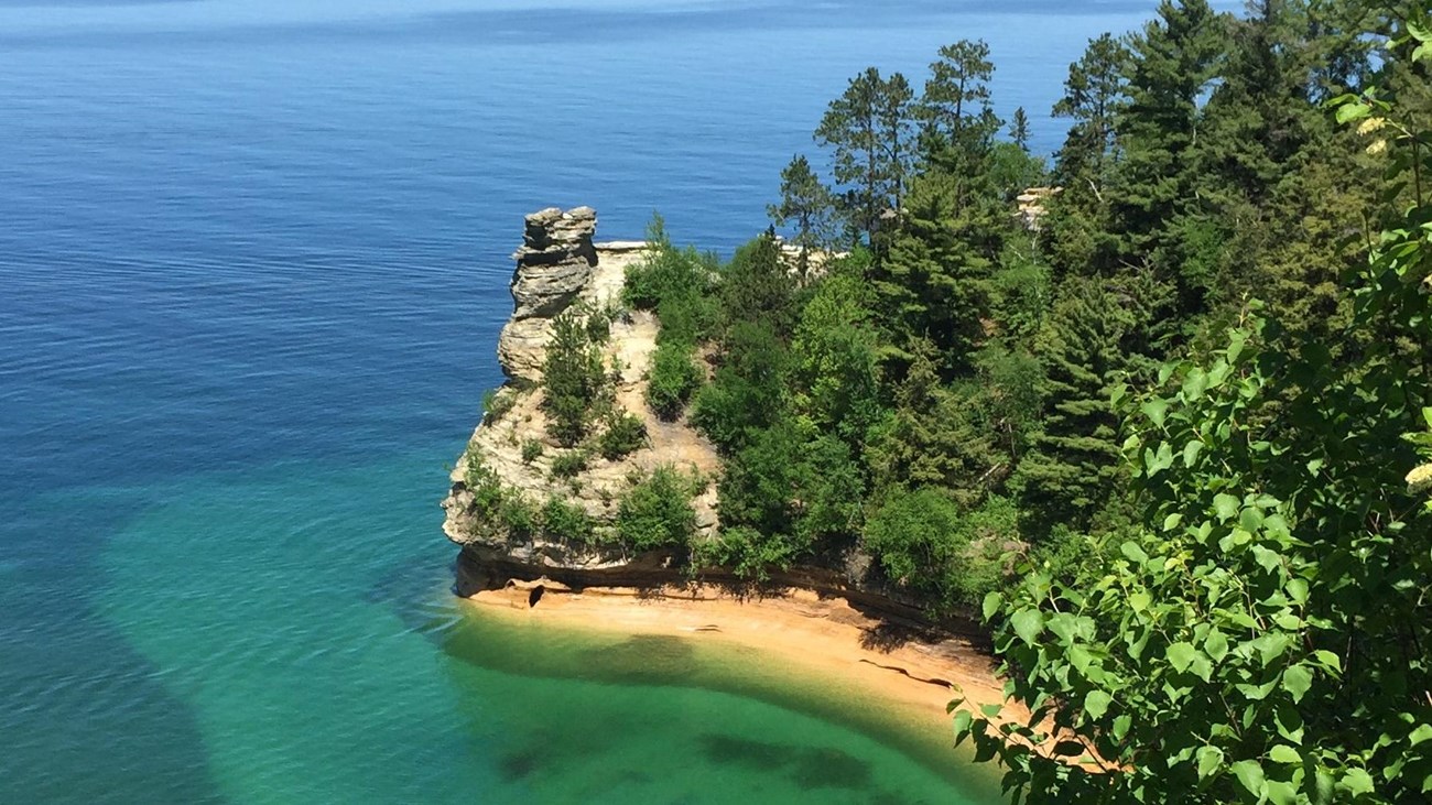 Rock formation of Miners Castle along cliffline above multi-colored Lake Superior water.