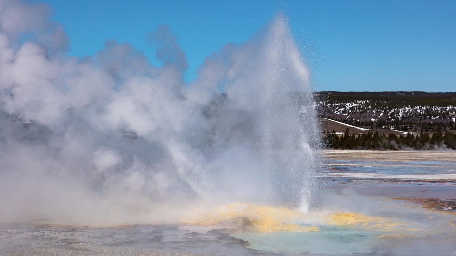 A geyser erupts from a small pool, spraying water and steam into the air.